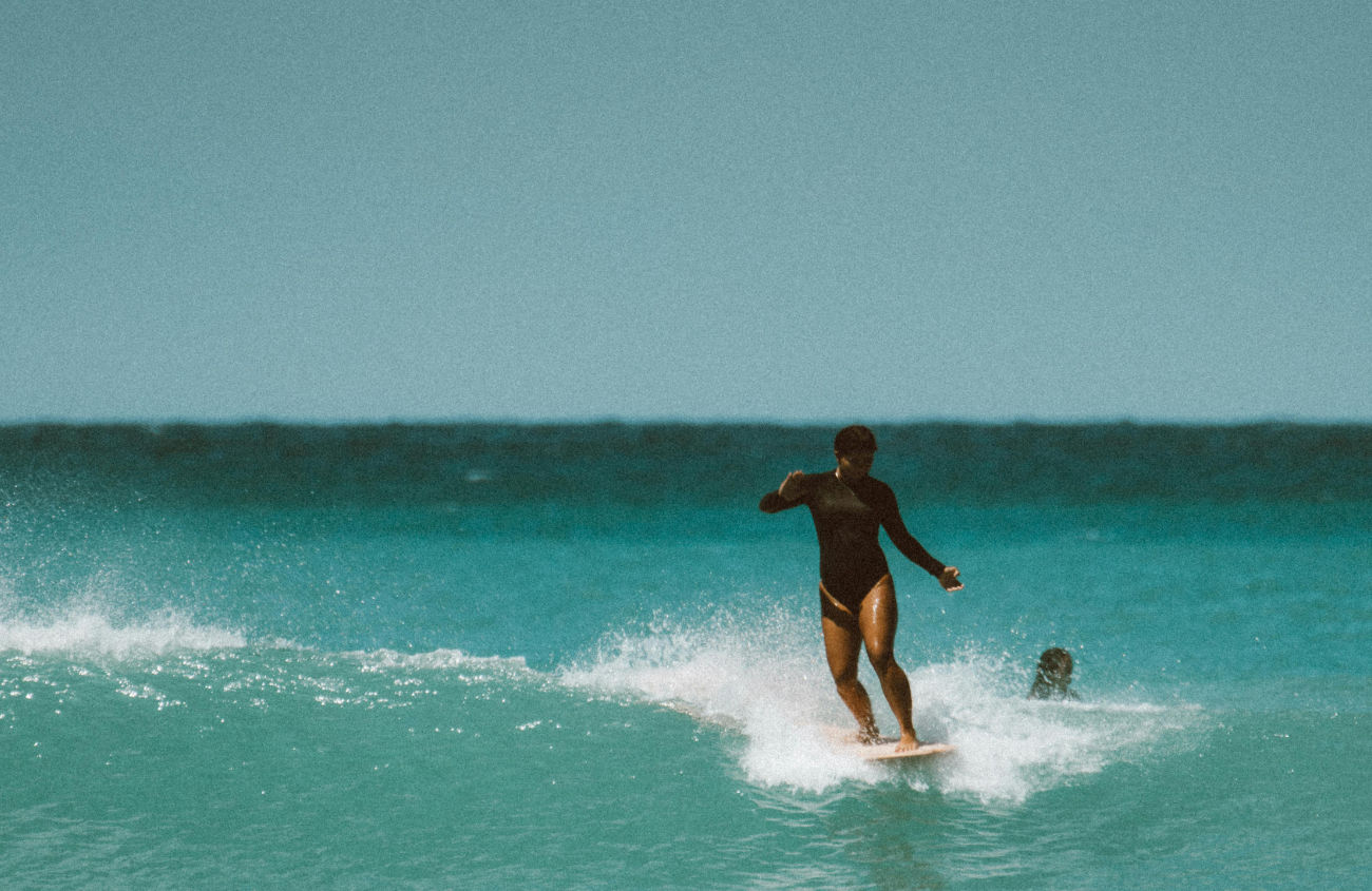 A surfer in the ocean, riding a wave, embodying the sense of freedom and flow that is central to A NEW DAY's philosophy.